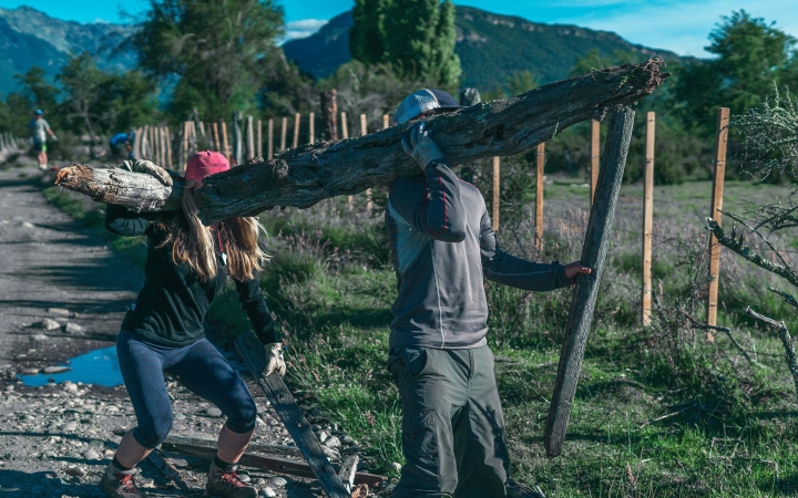 Two people carry a large piece of wood during a service project with outward bound. 